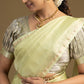 Woman wearing a light green saree with gold jewelry against a beige background