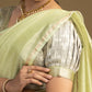 Woman wearing a light green saree with gold jewelry against a neutral background