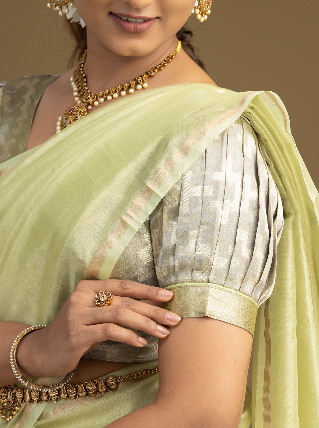 Woman wearing a light green saree with gold jewelry against a neutral background