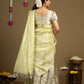 Woman wearing a light green saree with a white blouse against a brown background