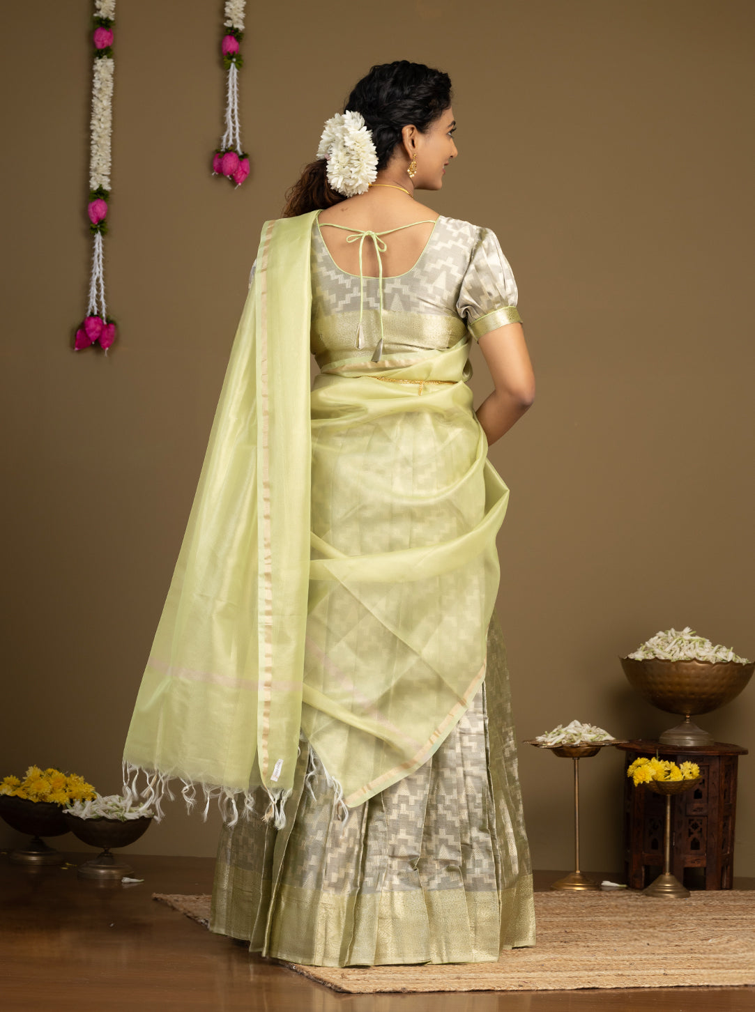Woman wearing a light green saree with a white blouse against a brown background